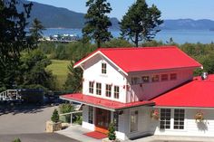 a large white house with a red roof next to some trees and mountains in the background