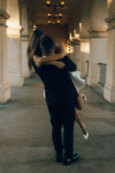 a man and woman embracing in an old building with columns on either side of them