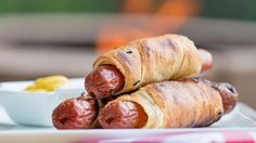 two sausages wrapped in bacon sitting on a plate next to a bowl of mustard