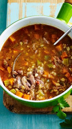 a bowl of soup with meat and vegetables in it on a table next to a spoon