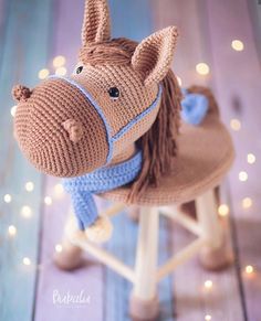 a knitted toy horse sitting on top of a wooden stool next to christmas lights