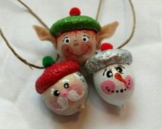 three christmas ornaments are hanging on a white sheet with snowman and elf faces painted on them