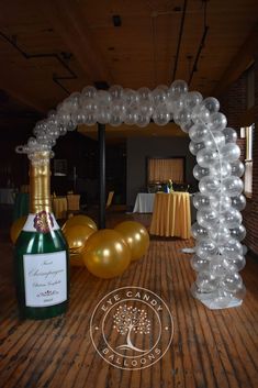 an arch made out of balloons with a bottle of champagne in front of it on a wooden floor