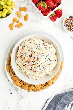 a bowl filled with white frosting surrounded by crackers and strawberries