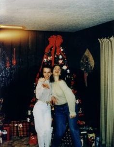 two people standing in front of a christmas tree