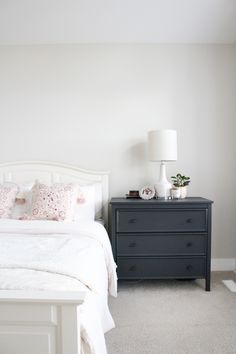 a white bed sitting next to a black dresser in a bedroom on top of a carpeted floor