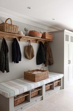 a white bench sitting next to a wooden shelf filled with baskets and coats on top of it