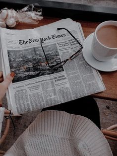 a person reading the new york times newspaper next to a cup of coffee