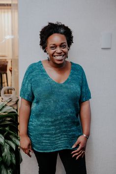 a woman standing next to a potted plant in front of a white wall smiling