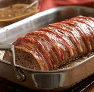 meatloaf covered in bacon sitting on top of a metal pan with tongs