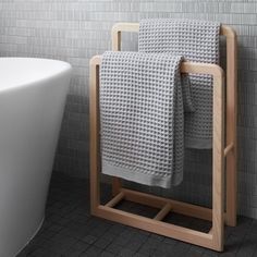 a white bath tub sitting next to a wooden stand with two towels on top of it