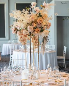 a tall vase filled with lots of flowers on top of a white table cloth covered table