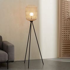 a floor lamp sitting on top of a metal tripod next to a gray couch