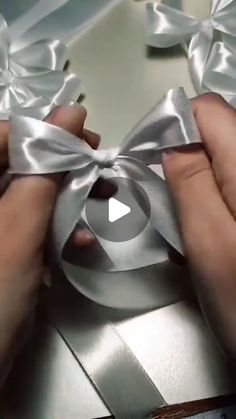 two hands are tying the ribbon on a silver gift box with white satin ribbons and scissors