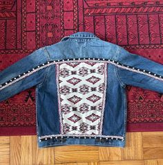 "Welcome to my collection of upcycled clothing! :) Every piece is made with items thrifted or upcycled for the purpose of creating sustainable pieces and decreasing waste! Handmade and Upcycled Fabric and trims with Aztec patterns have been hand-sewn along with a layer of silver tone sequins to transform this denim jacket with a chic BOHO look!  SIZE: It says Kids XL but MAY easily fit a regular women's size 6-8 Chest: 36\" Sleeve Length: 21\" Shoulder: 16.5\" Jacket Length: 22\" Care Instructions: This garment has handsewn details. I recommend gentle hand washing with mild detergent. DO NOT SOAK for more than 15 minutes in cold water. Do not wash with fabric softener or bleach. Lay flat or hang dry. Iron on the reverse side." Bohemian Embroidered Denim Outerwear, Bohemian Embroidered Outerwear In Medium Wash, Bohemian Denim Jacket With Pockets In Medium Wash, Bohemian Medium Wash Long Sleeve Outerwear, Bohemian Long Sleeve Outerwear In Medium Wash, Bohemian Long Sleeve Medium Wash Outerwear, Bohemian Embroidered Cotton Denim Jacket, Bohemian Medium Wash Cotton Outerwear, Custom Jean Jacket