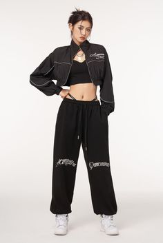 a woman standing in front of a white background wearing black sweatpants and crop top