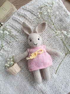 a knitted bunny doll laying on top of a white blanket next to some flowers