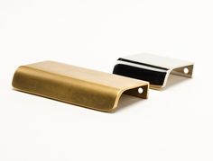 two brass and black metal objects on a white surface, one is folded up to the side