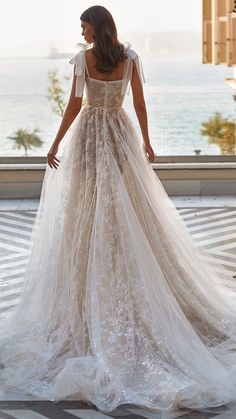 a woman in a wedding dress looking out the window at the water and buildings behind her