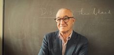 an older man wearing glasses standing in front of a blackboard