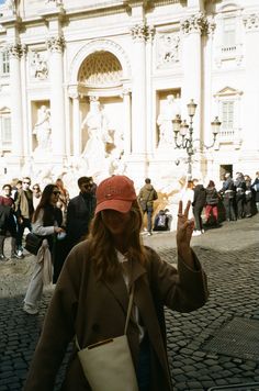 a woman wearing a red hat and brown coat standing in front of a white building