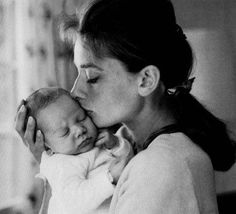 a woman holding a baby in her arms and kissing it's face with the other hand