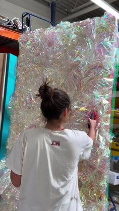 a woman in white shirt standing next to a large pile of plastic wrappers