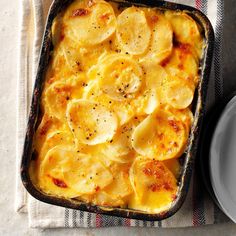 a casserole dish with potatoes and cheese on a striped cloth next to a plate