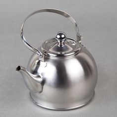 a silver tea pot with a metal handle on a gray background, the kettle has a ball at the top