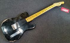 an old black guitar sitting on top of a gray floor next to a red and white tag