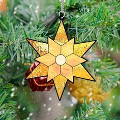 a stained glass star ornament hanging on a christmas tree branch with snow falling around it