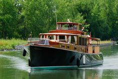 a large boat traveling down a river next to lush green trees