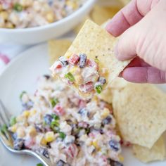 a hand holding a tortilla chip with black beans and corn salad on it