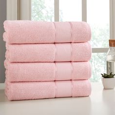 a stack of pink towels sitting on top of a counter next to a potted plant