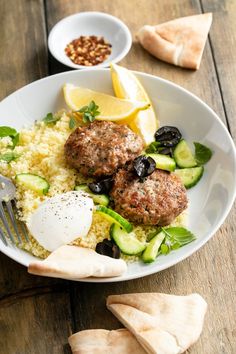 a white plate topped with meatballs, rice and cucumbers next to lemon wedges