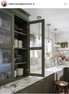 a kitchen with green cabinets and marble counter tops, along with an open glass door