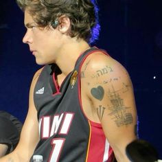 a young man with tattoos on his arm and shoulder sitting in front of a microphone