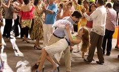 a man and woman dancing in front of a group of people on the street with their arms around each other