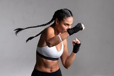 a woman wearing black and white boxing gloves with her arm wrapped around the wrist, posing in front of a gray background