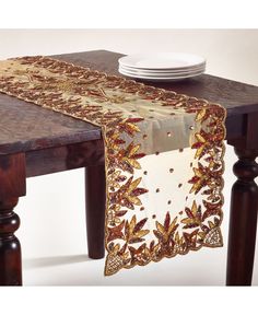 a wooden table topped with a white plate next to a brown and gold table runner