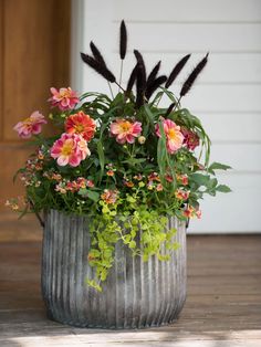 a metal planter filled with lots of flowers on top of a wooden floor next to a door