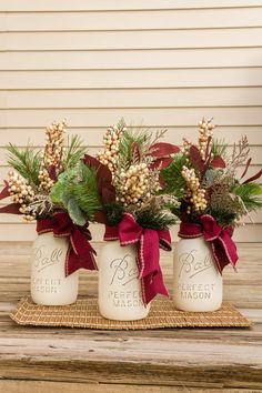 three white mason jars with red bows and greenery are sitting on a wooden table