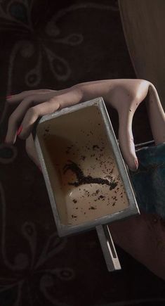 a woman holding a box with dirt on it and her hand reaching out to the ground