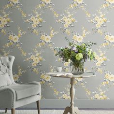 a white chair sitting next to a table with flowers on it in front of a yellow wall