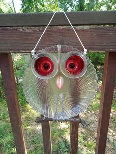 a glass owl with red eyes hanging from a wooden fence