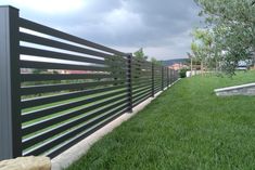 a black metal fence in the middle of a grassy area next to a stone wall