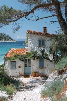 an old white house sitting on top of a sandy beach next to the ocean and trees