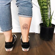 a woman's foot with a flower tattoo on her left leg, next to a potted plant