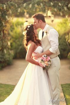 a bride and groom kissing in front of an arch with flowers on it at their wedding