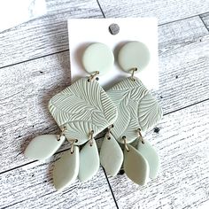 a pair of white earrings sitting on top of a wooden floor next to a card